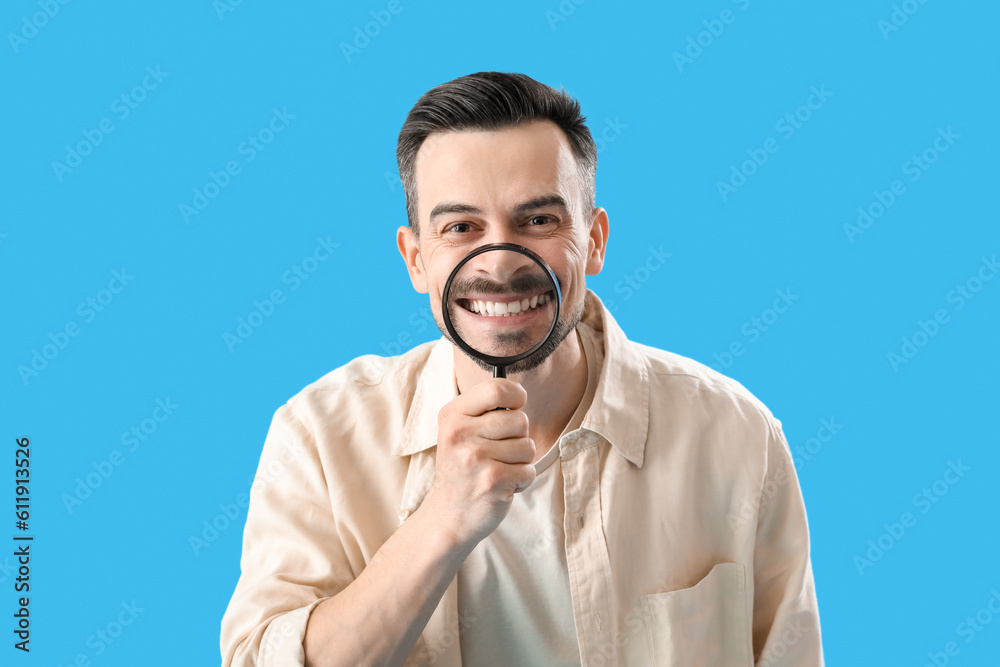 Handsome man with magnifier on blue background