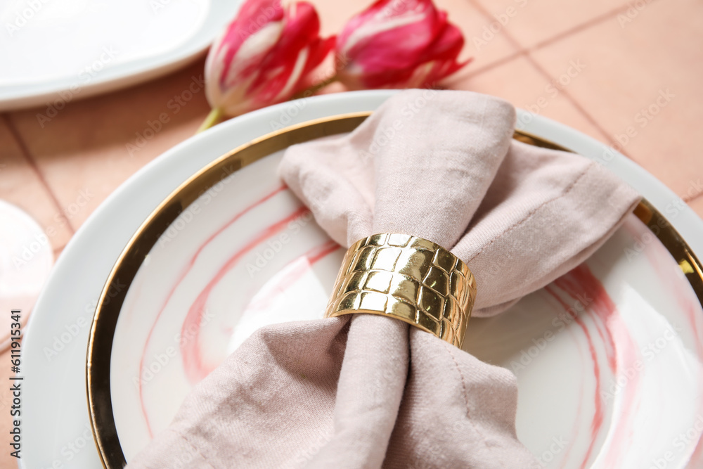 Plates with folded napkin, cutlery and tulip flowers on pink tile background