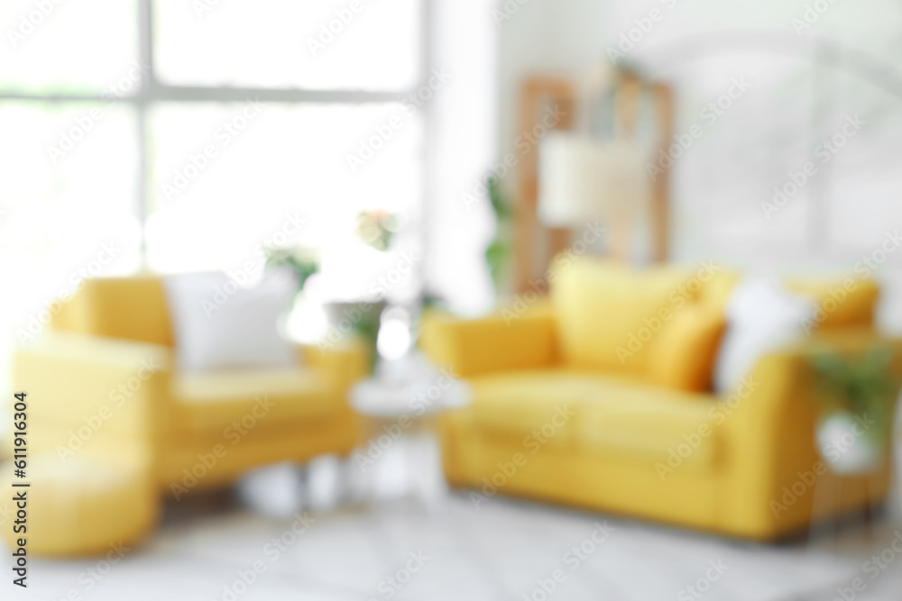 Interior of light living room with yellow sofa and armchair near big window, blurred view