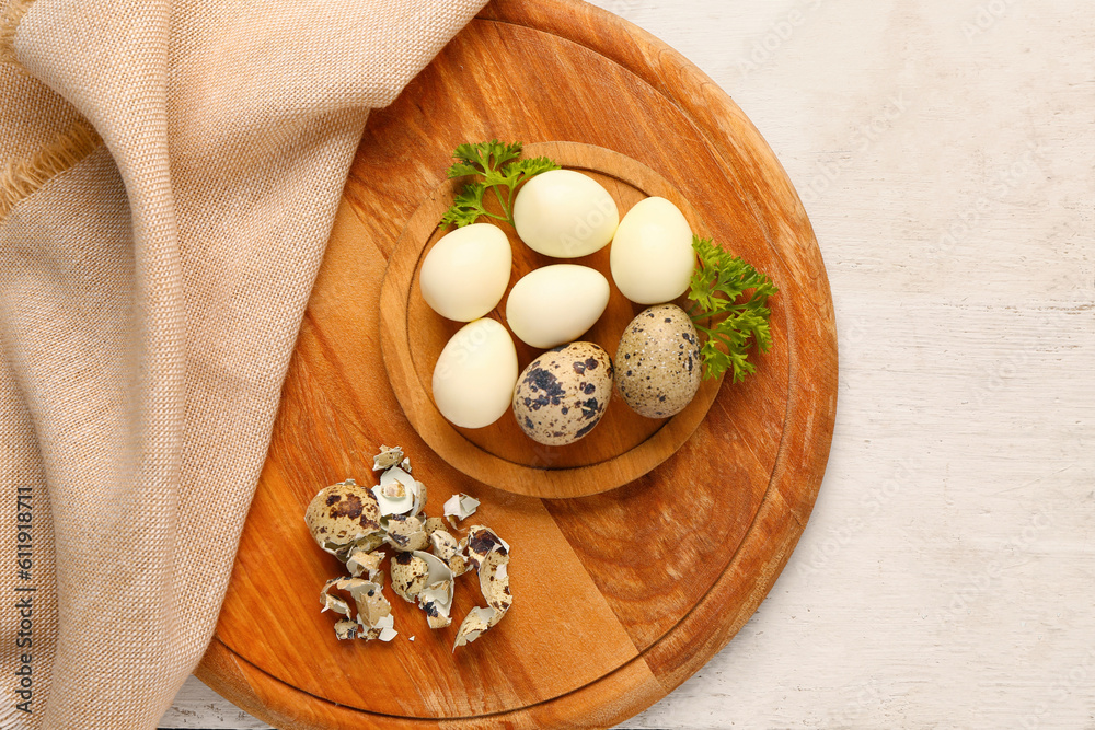 Board of boiled quail eggs with shells on white wooden background