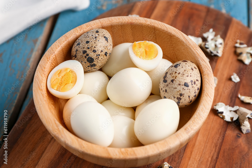 Board with bowl of boiled quail eggs and shells on blue wooden background