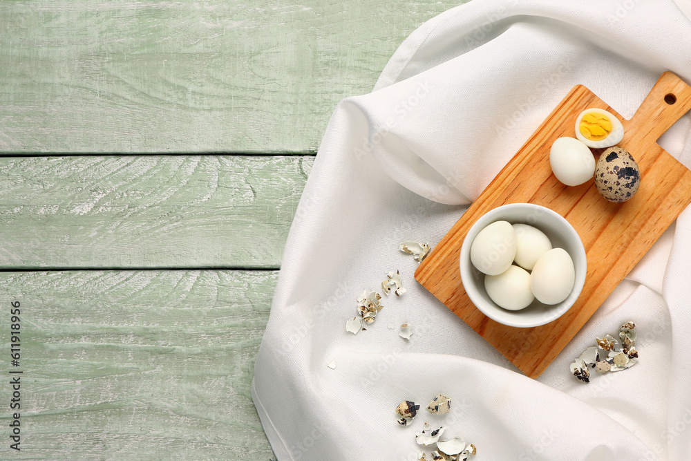 Board with bowl of boiled quail eggs and shells on green wooden background