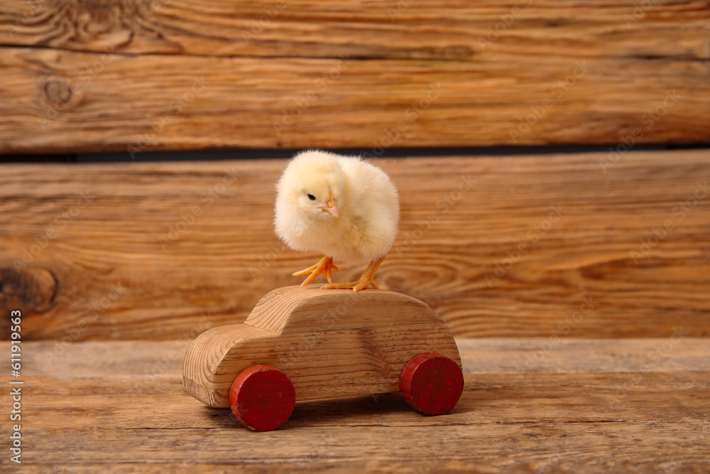 Car figure with cute little chick on wooden background