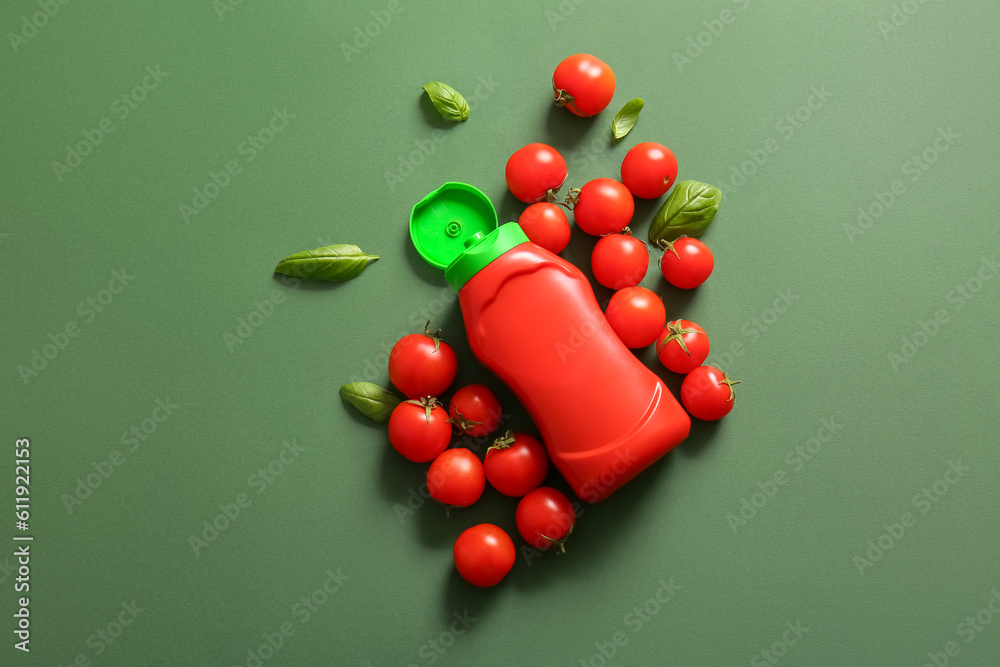 Bottle of ketchup and tomatoes on green background