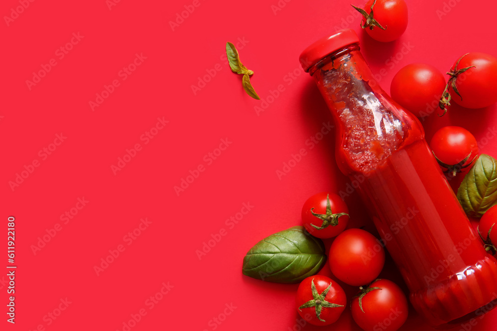 Glass bottle of ketchup and tomatoes on red background