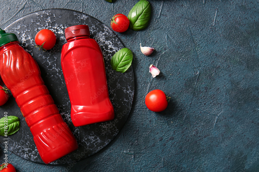 Board with bottles of ketchup and tomatoes on dark background