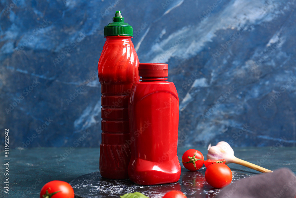 Bottles of ketchup and tomatoes on blue background