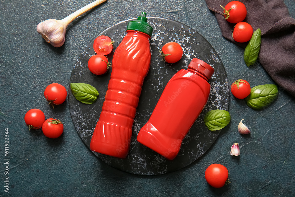 Board with bottles of ketchup and tomatoes on dark background