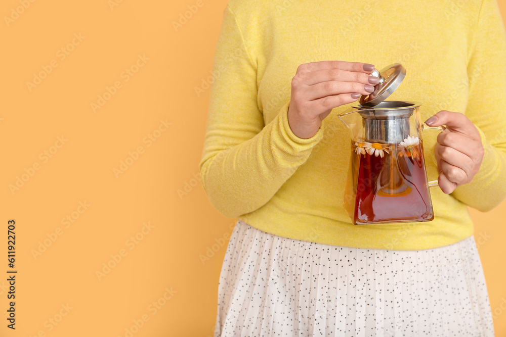 Beautiful young woman with teapot of chamomile tea near yellow wall