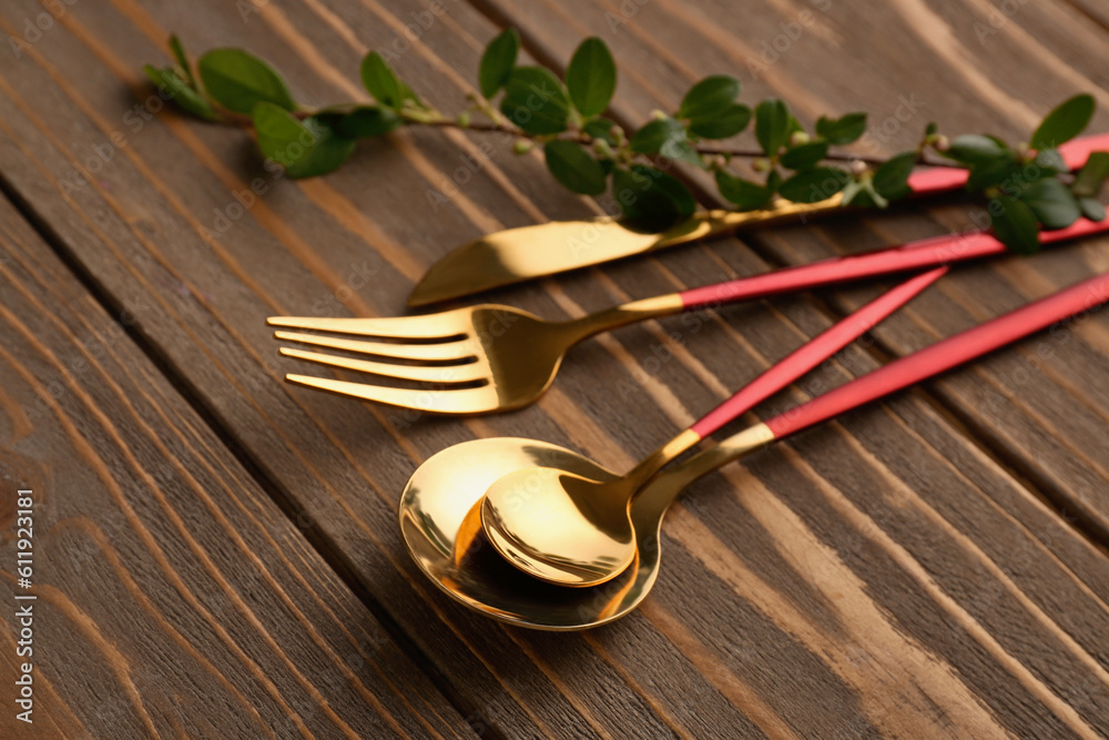 Golden cutlery with red handle and cotoneaster twig on wooden background