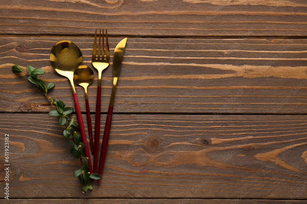 Golden cutlery with red handle and cotoneaster twig on wooden background