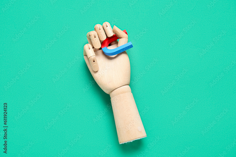 Wooden hand with horseshoe shaped mini magnet on green background