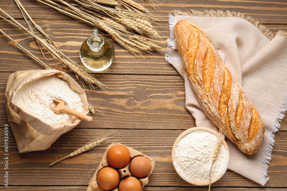 Frame made of fresh bread, eggs, oil and paper bag with wheat flour on brown wooden background