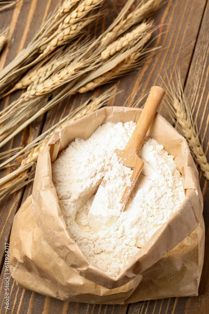 Paper bag with flour and wheat ears on brown wooden background