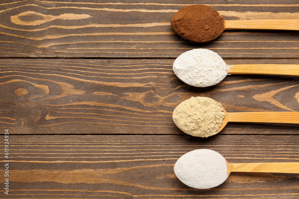 Wooden spoons with different types of flour and cacao on brown wooden background