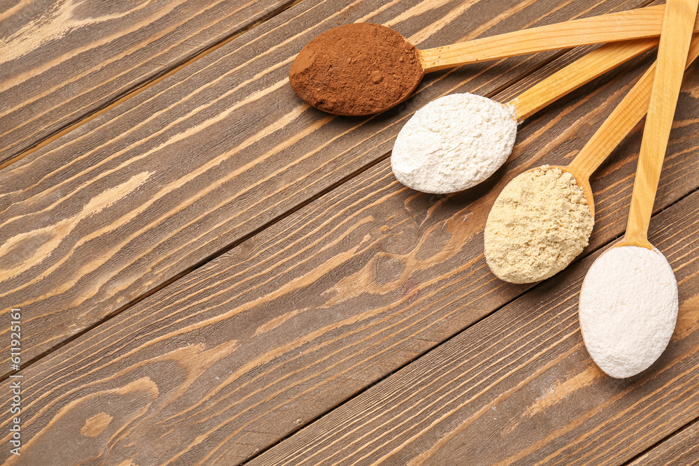 Wooden spoons with different types of flour and cacao on brown wooden background