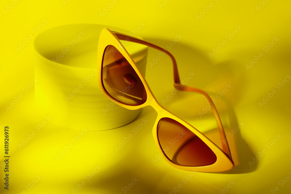 Podium with stylish sunglasses on yellow background