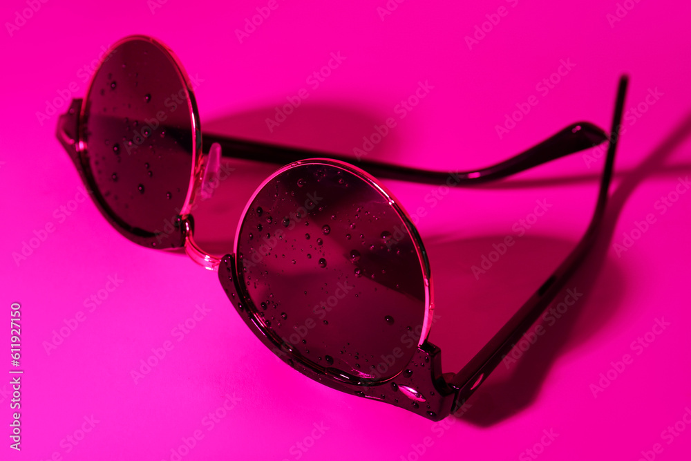 Stylish sunglasses with water drops on pink background