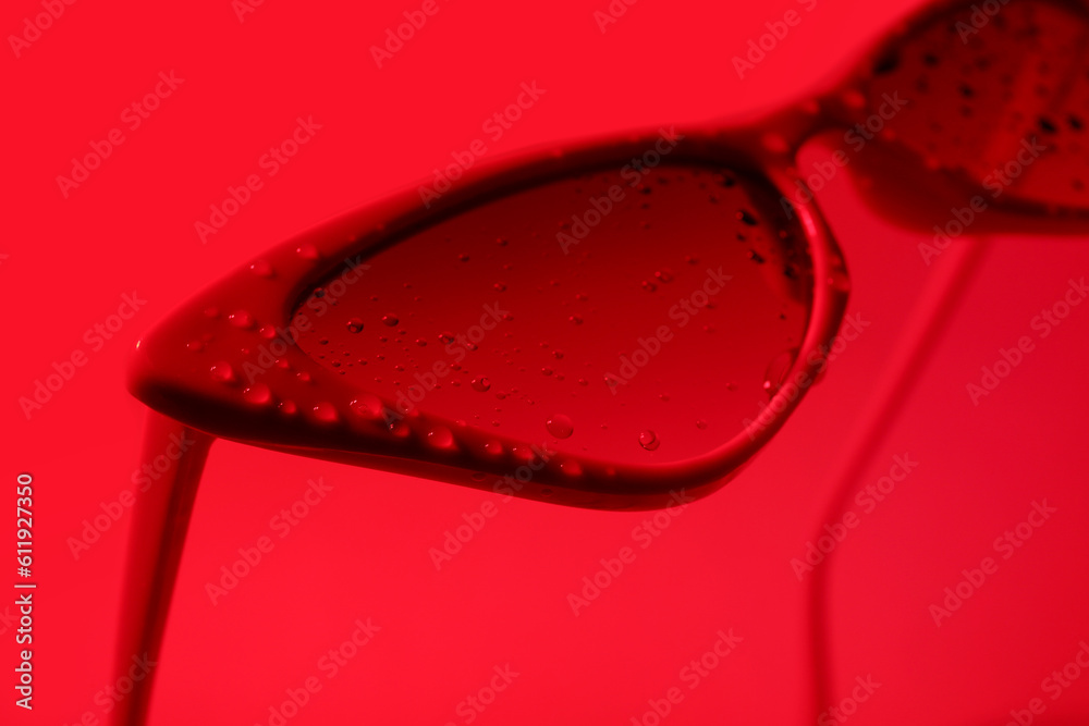 Stylish sunglasses with water drops on red background