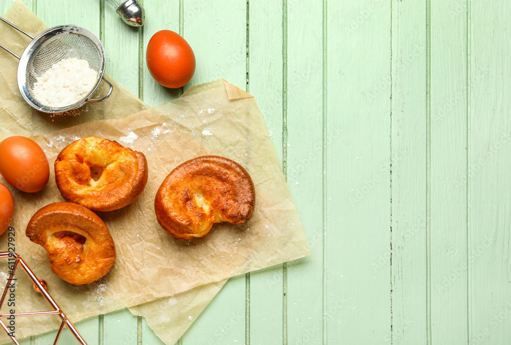 Tasty Yorkshire pudding and ingredients on green wooden background