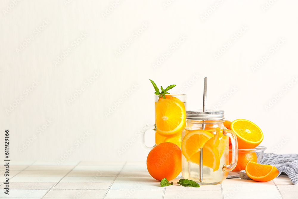 Mason jar and glass of infused water with orange slices on white tile table