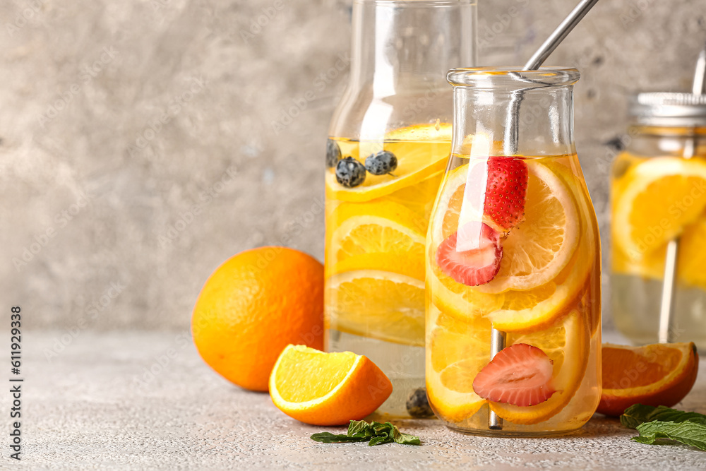 Bottles and mason jar of infused water with orange slices on grey table