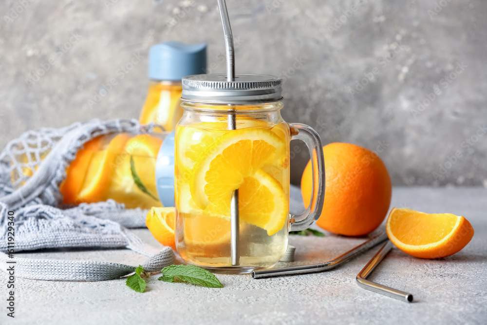 Mason jar and sports bottle of infused water with orange slices on grey table