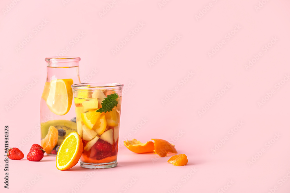 Glass and bottle of infused water with different sliced fruits on pink background