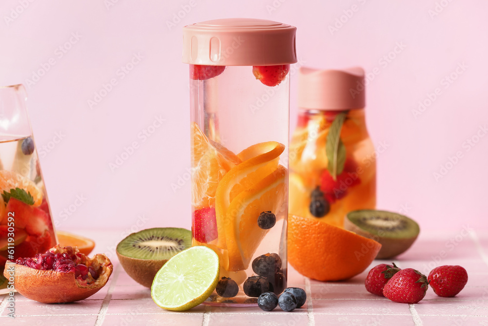 Sports bottles of infused water with different sliced fruits on pink tile table