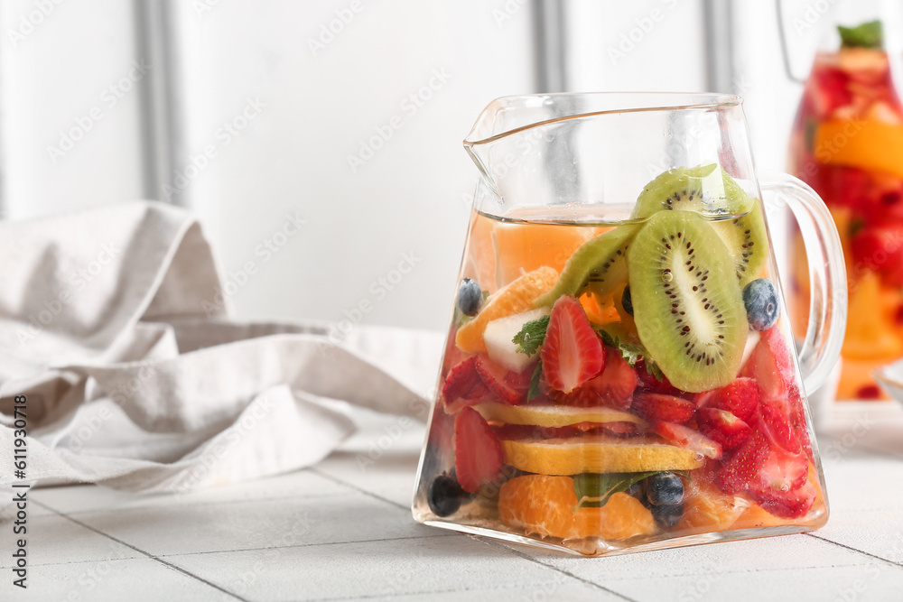 Jug and bottle of infused water with different sliced fruits on white tile table