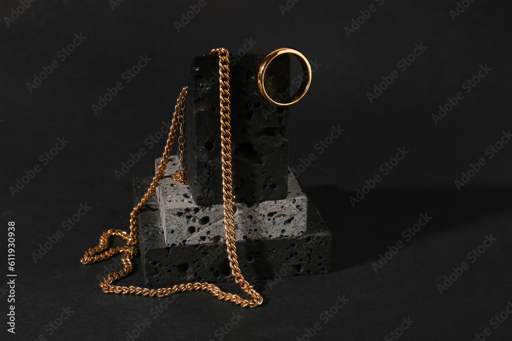 Decorative podium with beautiful chain necklace and ring on black background