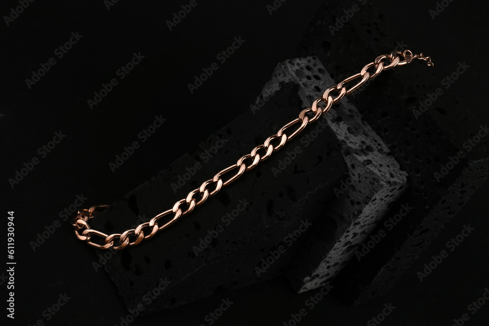 Decorative podium with beautiful chain bracelet on black background