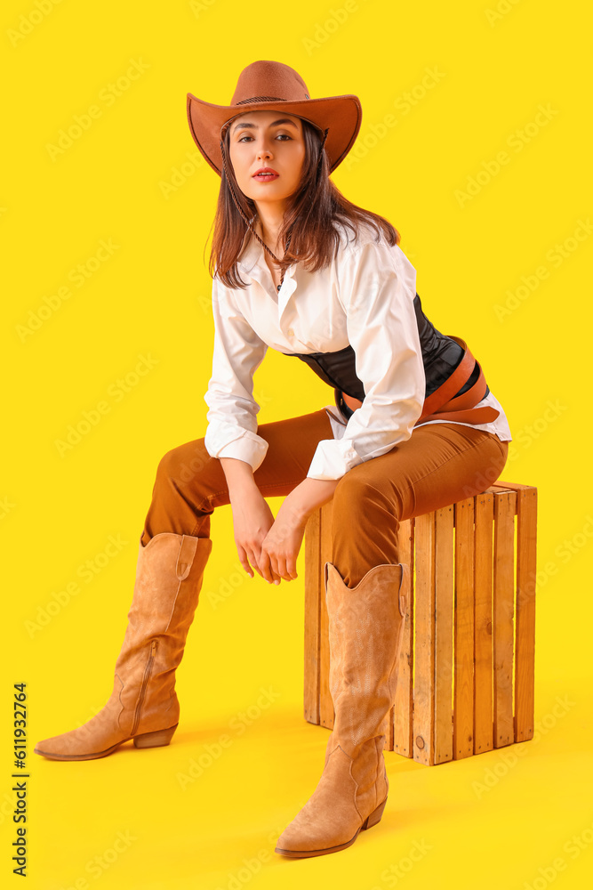 Beautiful cowgirl sitting on yellow background