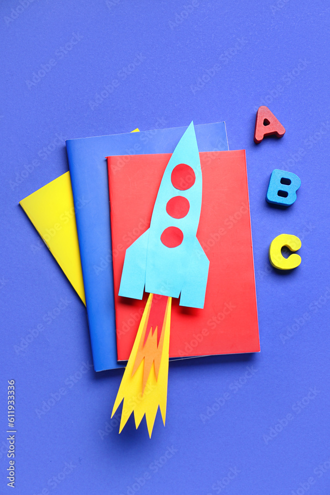 Paper rocket with notebooks and wooden letters on dark blue background