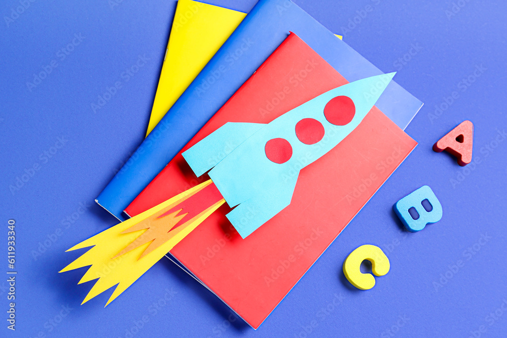 Paper rocket with notebooks and wooden letters on dark blue background