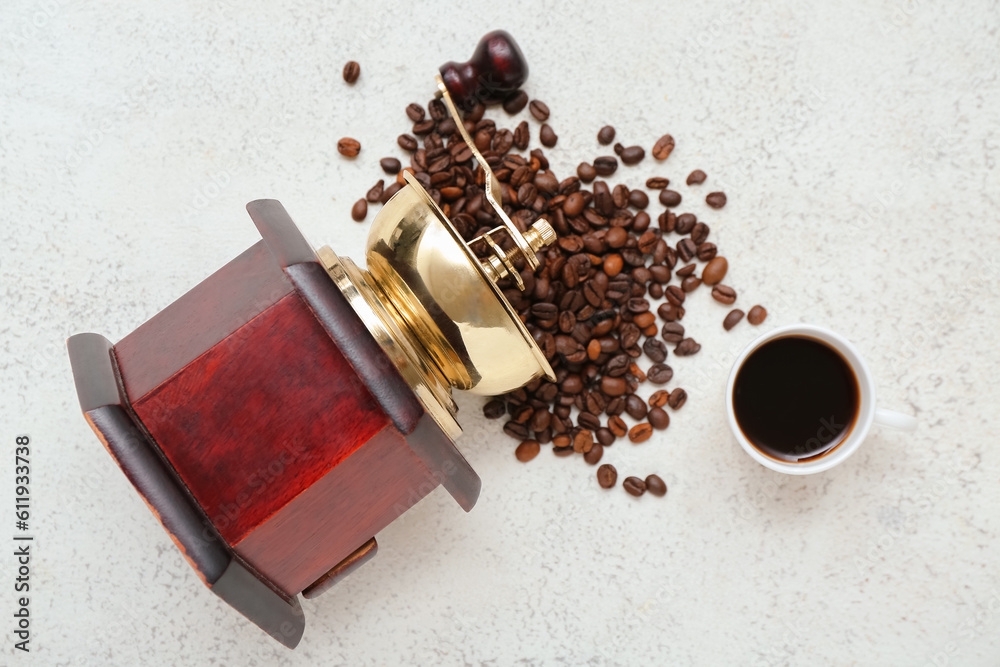 Cup of hot espresso and coffee grinder with beans on light background