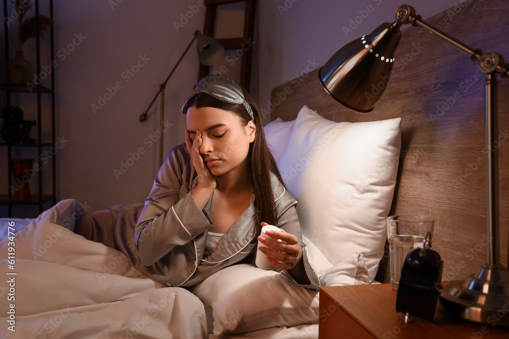 Young woman taking pill bottle in bedroom at night