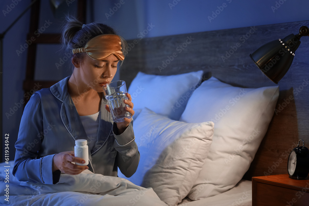 Young woman with pill bottle and glass of water in bedroom at night