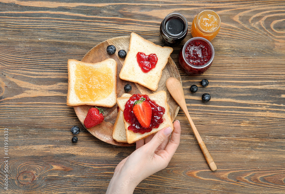 Woman holding delicious toast with strawberry jam and berries on brown wooden background