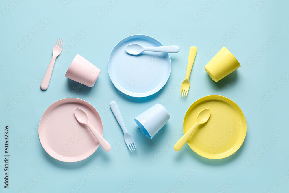 Plates with cups and cutlery for baby on blue background