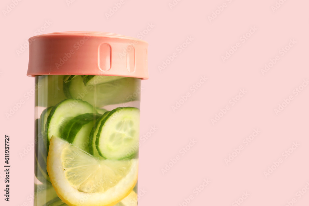 Sports bottle of infused water with cucumber slices on pink background