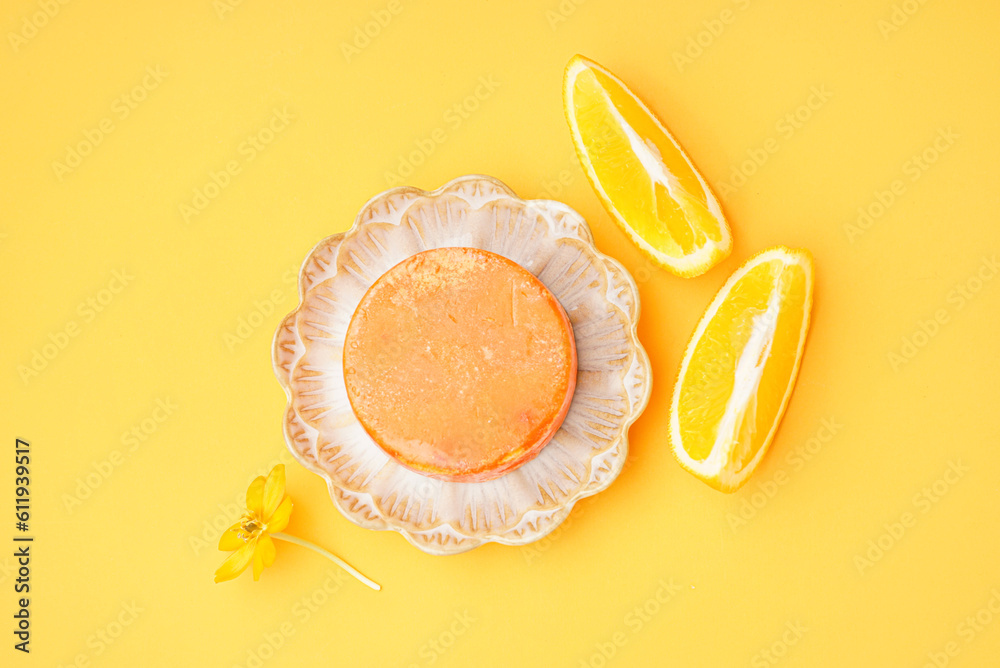 Plate with solid shampoo bar, flower and orange on color background