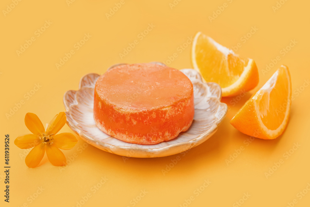 Plate with solid shampoo bar, flower and orange on color background