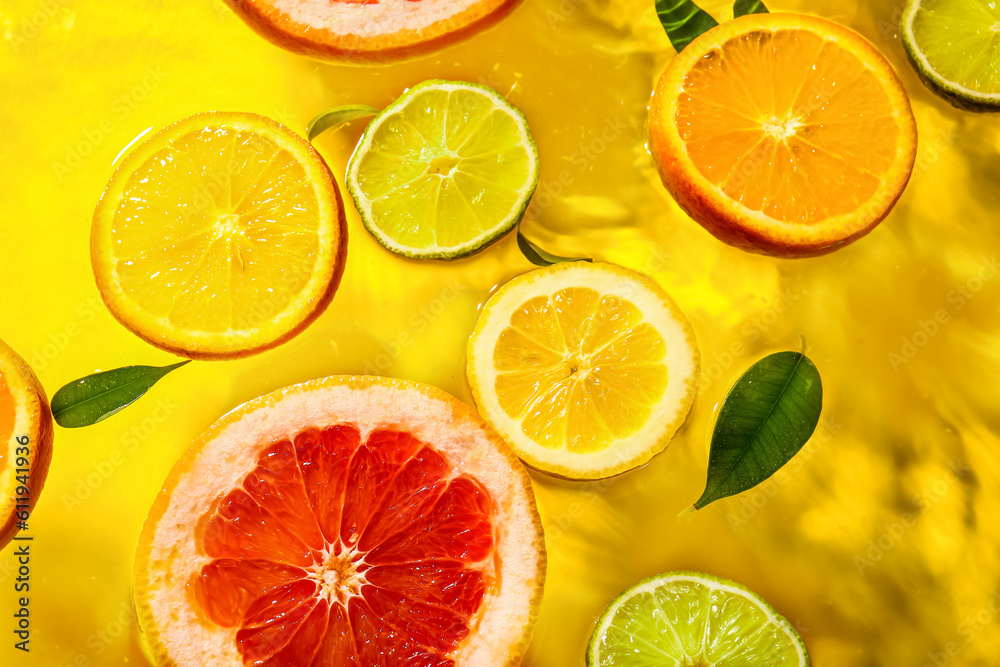 Different citrus fruit slices and leaves in water on yellow background