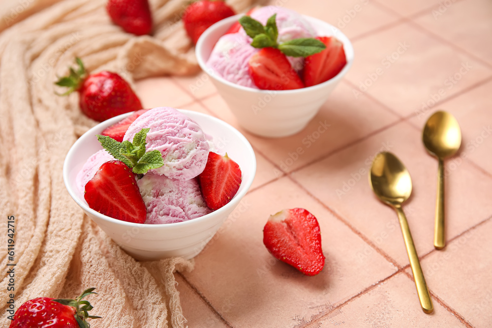 Bowls of strawberry ice cream with berries, mint and golden spoons on beige tile table