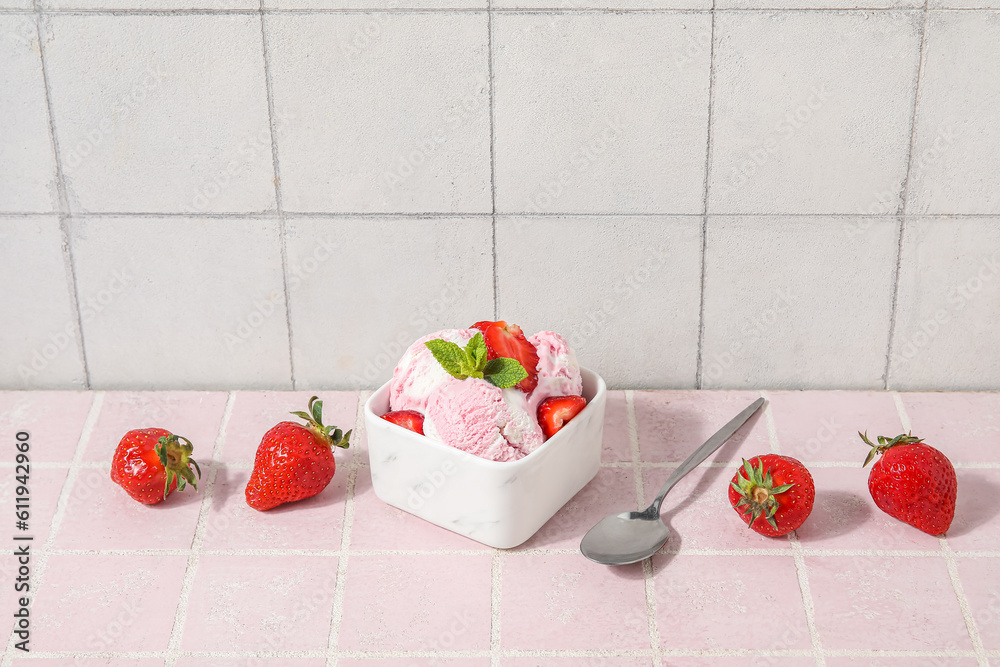 Square bowl of strawberry ice cream with mint, berries and spoon on pink tile table near white wall