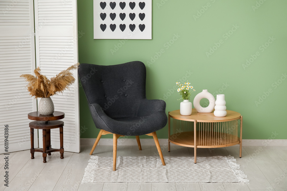 Dark grey armchair with dressing screen, coffee tables and vases near green wall