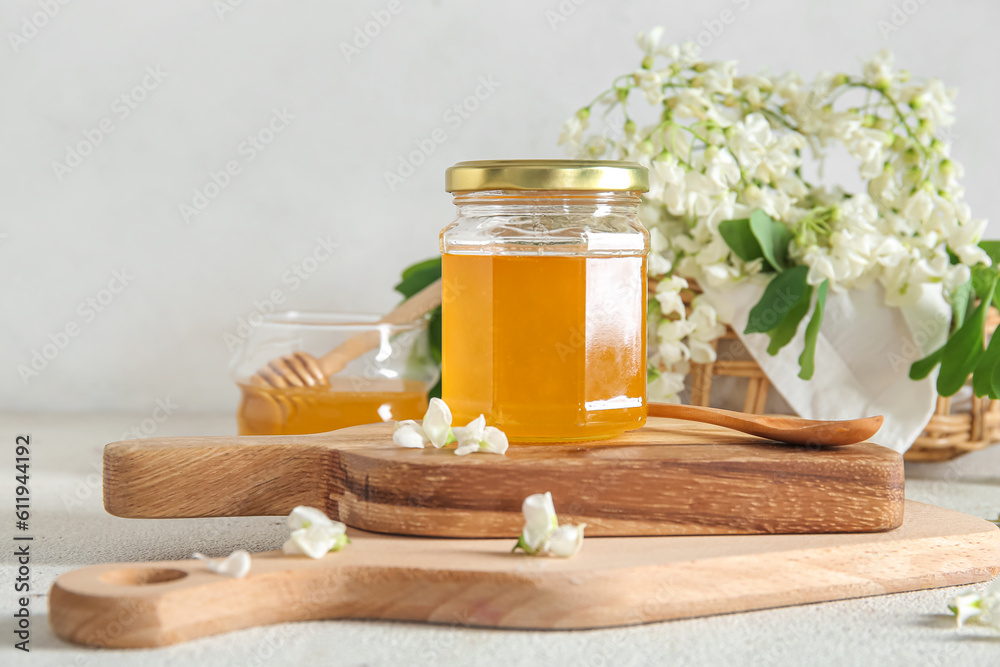 Jar of honey with flowers of acacia on light background, closeup