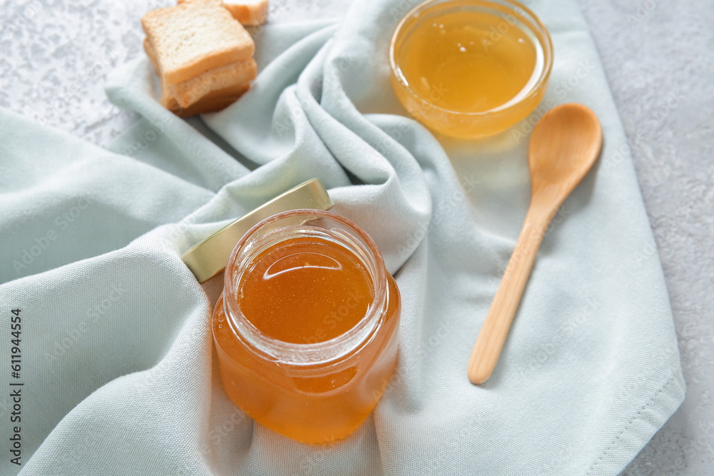 Jar of acacia honey and crackers on light background, closeup