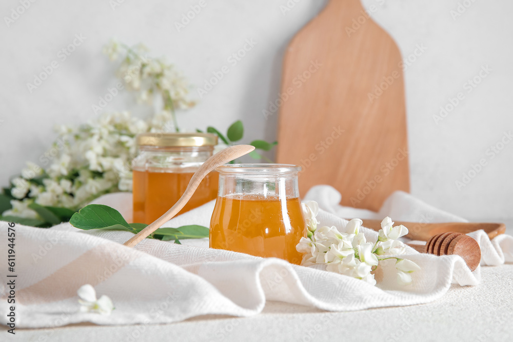 Jars of honey with flowers of acacia on light background